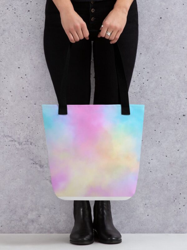 A person holding a pastel-colored tote bag with a soft, cloud-like pattern reminiscent of the aurora borealis, against a grey concrete background, illustrating the bag's practicality and aesthetic appeal.