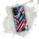 An image of a ZestFiesta Clear Case for a Samsung® smartphone, featuring a bright, abstract geometric pattern with sharp angles in pink, blue, yellow, and black on a transparent background. The case has precise cutouts for the phone's cameras and buttons, and is shown partially submerged in a white liquid, suggesting water resistance.