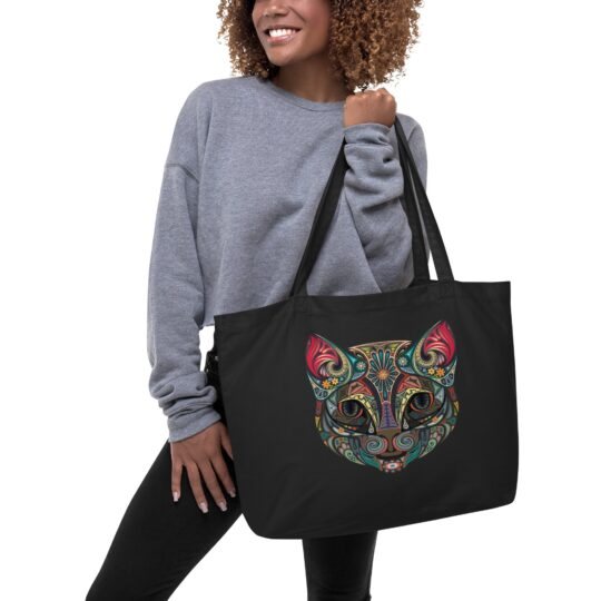 A person holding a black organic tote bag adorned with a colorful tribal cat design.