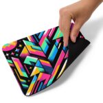 A hand resting on a ZestFiesta Mouse Pad, which displays a vivid geometric pattern in bright shades of pink, blue, yellow, and black, providing a colorful and dynamic surface for mouse usage.